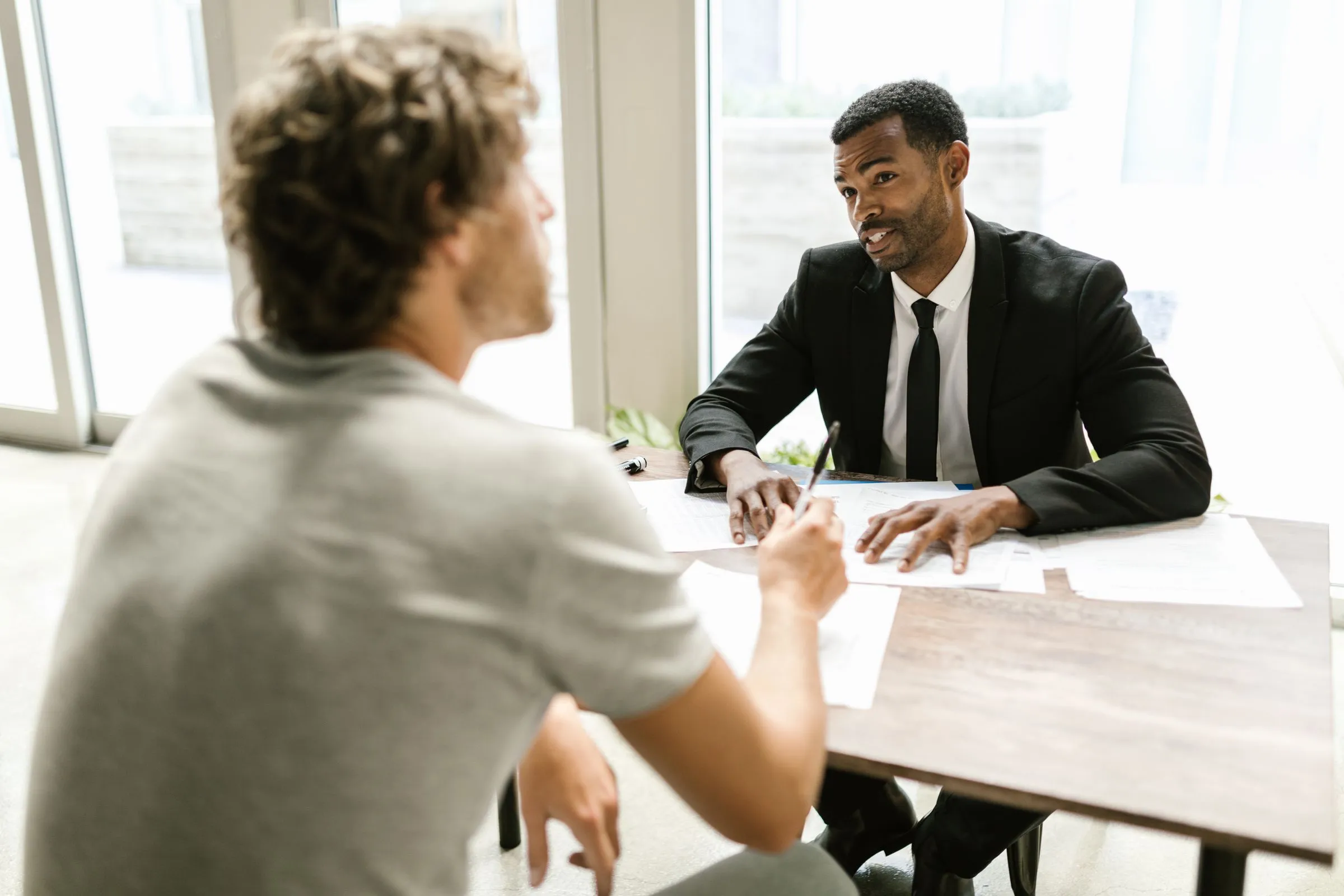 Consultor de terno conversa com um cliente sobre documentos em uma mesa de escritório